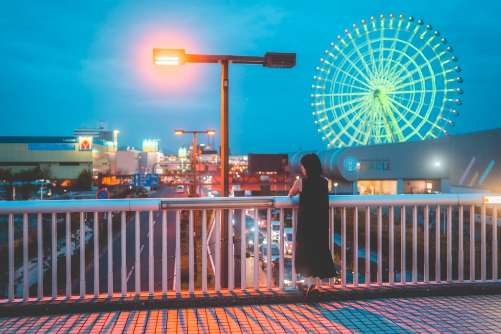 都会的な夜の写真。女性が橋の上に立ち、背をこちらに向けている。