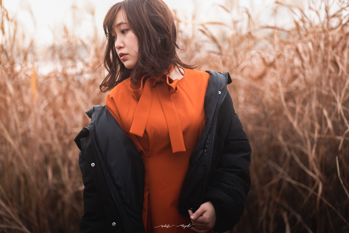 女性のポートレート写真。オレンジのワンピースとジャケットを着ている。