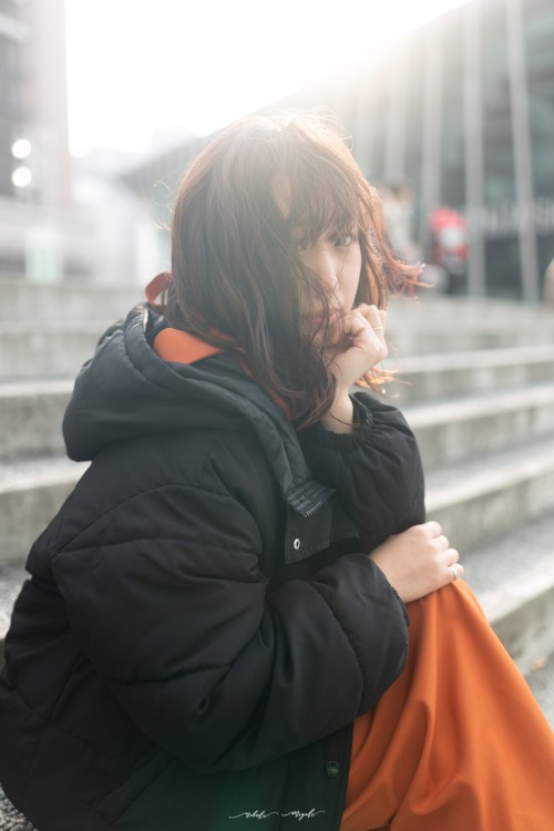 女性モデルの写真。オレンジ色の衣装を着て、コートを羽織っている。